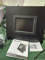 Front of the Siren 5-inch digital photo frame with Quick Start Guide pamphlet placed in front of it.