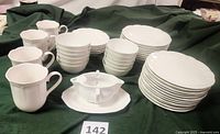 Wide view of all Studio Nova HG300 White Rose plates, bowls, mugs, dessert bowls, and porcelain gravy separator with underplate arranged on green cloth