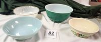 Four vintage oven-safe bowls of various colors and brands arranged on white fabric with dark green cloth background.