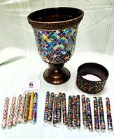 Photo shows the vintage mosaic stained glass candle holder with bronze base alongside the jeweled pen cup. Twenty jeweled pens are arranged beside them, mostly with multi-colored beading and jewel caps in clear plastic tubes.