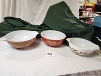 Three vintage Pyrex mixing bowls arranged side by side on white surface with green cloth background.