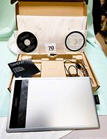 Wacom Bamboo tablet and accessories laid inside original box, including pen, two CDs, pamphlet, USB cord