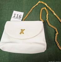 Front view of the white leather bag showing the artistic gold X closure and gold heavy chain strap.