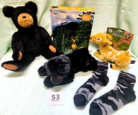Full lot with all items laid out on table showing the large black plush bear, smaller sleeping bear, deer puzzle, camouflage socks, and yellow deer plush.