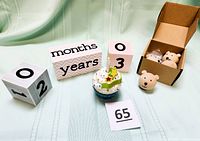 Wooden baby milestone blocks with one cube showing '02', the rectangular piece with 'months' and 'years', the number '03' cube, plus ceramic cupcake figurine and one detached mini bear head hook with other hooks in box