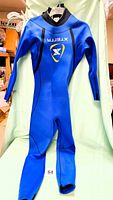 Blue full wetsuit hanging, front view showing XTERRA logo on chest, high collar, and long sleeves and legs.