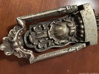 Top view of the ornate cast iron door knocker showing detailed design with floral or shield motif and a heavy, solid structure.