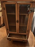 Front view of the antique wooden vitrine cabinet showing double glass doors and an open drawer below.