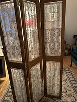 Close-up of lace fabric panels on antique wood frame, showing floral lace pattern and wood grain details.