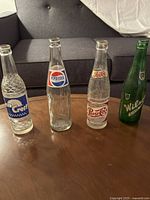 Four antique soda bottles: Sun Crest, Pepsi Cola (two different labels), and Wilson, displayed on a wooden surface.