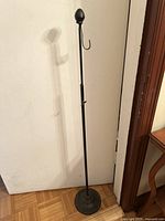 Full view of the black cast iron wreath holder showing its height, pineapple finial, single hook, and adjustable shaft.