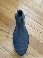 Top view photo of antique cast iron shoe form mold resting on wooden floor, showing foot shape and hollow base.