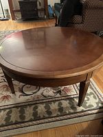 Top view of the round wooden coffee table in a living room setting, showing the smooth brown finish and subtle panel design on the tabletop.