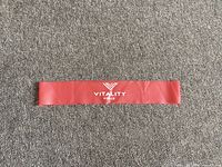 Photo showing entire red resistance band with 'Vitality Force' printed in white against a carpet floor.
