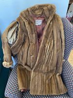 Full view of the brown 3/4 length mink fur coat laid over a chair showing the body and sleeves with visible rips and worn areas.