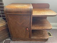 Side view of the wooden side table showing cabinet door and three open shelves with visible wear and aging.