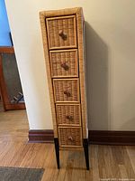 Side angle view of the other wicker drawer unit showing wicker construction and dark wooden legs.