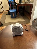 Portable white compact heater on a wooden round table, showing overall size and design.