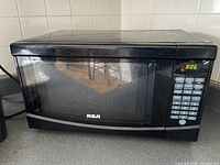 Front view of the black RCA microwave showing the transparent door and digital time display.