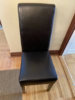 Front view of one black synthetic leather dining chair showing seat and high backrest with wooden legs.
