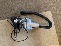 Silver Shark handheld vacuum with flexible hose and power cord on carpeted surface.