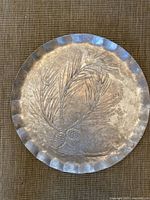 Full view of the round silver serving tray showing pine cone design and scalloped edge.