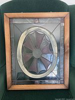 Framed stained glass panel on a green chair, showing the front view of the decorative panel with an oval and petal-like design.