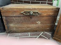 Front view of wooden storage chest showing metal handle and lock plate, scratches and wear on wood.