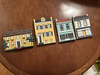 Four hand painted Victorian house plaques arranged on wood surface showing front details and colors.