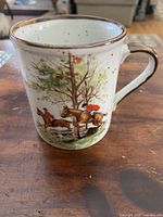 Single speckled stoneware mug shown from one side with horse rider in red jacket jumping over a fence among trees and dogs