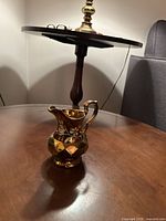 The creamer pitcher shown on a wooden table with a visible shiny copper lustre finish and floral design.