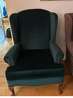 Front view of dark green wingback chair showing fabric upholstery, cushioned armrests, and wooden legs.