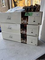 Three white boxes stacked, each labeled 'Cassandra' with image of single cut crystal glass and '4 bicchieri vasos copos'. The boxes have 'Regal Imports' logo and a green taped label '#54 12'.