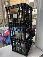 Stack of three black plastic milk crates showing lattice sides and open top, each capable of holding LP sleeves.