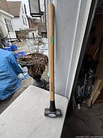 Full shot of the 8 LB sledge hammer, wooden handle, standing vertically outside on a table.