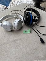 Two headphones side by side on a table, one white Sony and one black and blue headphone with microphone
