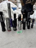 Front view of 15 assorted flashlights in varying sizes and colors on concrete surface with snow background.