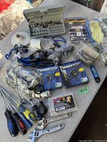 Wide view of lot showing assorted tools, adjustable wrenches, screwdrivers, spider cable organizers, socket bit set, and electrical hardware in plastic bags