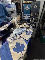 Overview photo showing multiple Toronto Maple Leafs memorabilia including flag, mugs, pucks, salt and pepper shakers, a collectible street sign, and a wall clock under outdoor lighting.