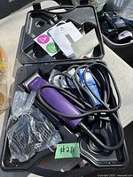 Purple Andis hair clipper with attached power cord, multiple clipper guards, instruction manual, all inside a black plastic carrying case.