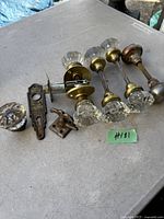 Photo showing four antique glass door knobs with brass bases mounted on spindles, along with three metal hardware parts including a backplate, latch, and strike plate.