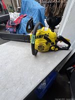 Side view of Champion 40cc chainsaw showing yellow body with branding and black padded handle.
