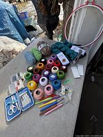 Overview of multiple skeins and balls of crochet and knitting threads on outdoor table, with several colorful crochet hooks laid beside them.
