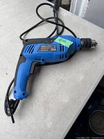 Full view of the corded blue and black electric hammer drill lying on a surface showing its overall design and condition.