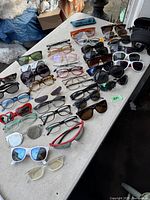 Photo of a wide variety of sunglasses and eyeglasses laid out on a white table showing diversity of frame styles and colors.