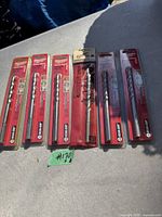 Six Milwaukee packaged drill bits laid out on a surface in sunlight, showing consistent packaging and identical items.