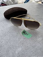 Photo shows a pair of unisex Celine Dion sunglasses with gold-toned metal frames and brown gradient lenses, placed on a grey surface with a brown sunglasses case in the background.