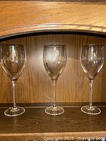 Three clear Christofle Albi white wine glasses on a wooden shelf, showing shape and size of the glasses.