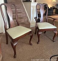 Two wooden dining chairs shown side by side, one with armrests and one without. Both have upholstered cushioned seats in light beige and carved legs.