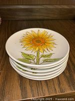 Stack of six circular appetizer plates with sunflower pattern displayed on a wooden surface.